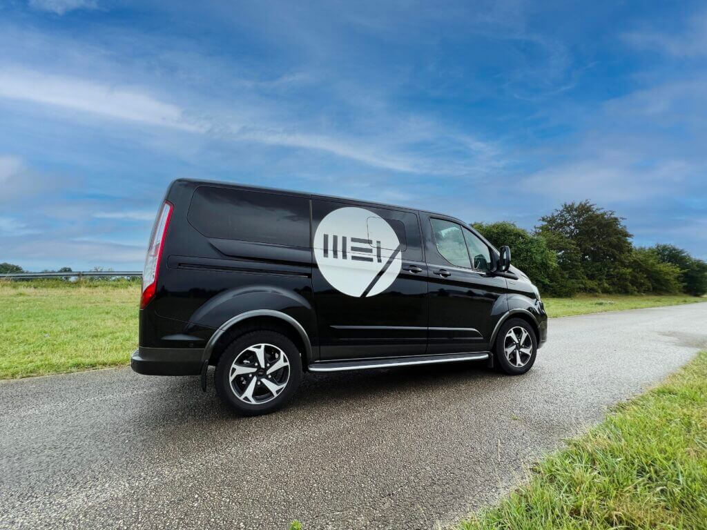 Schwarzer Transporter mit großflächiger weißer Fahrzeugbeschriftung auf der Seitenfläche