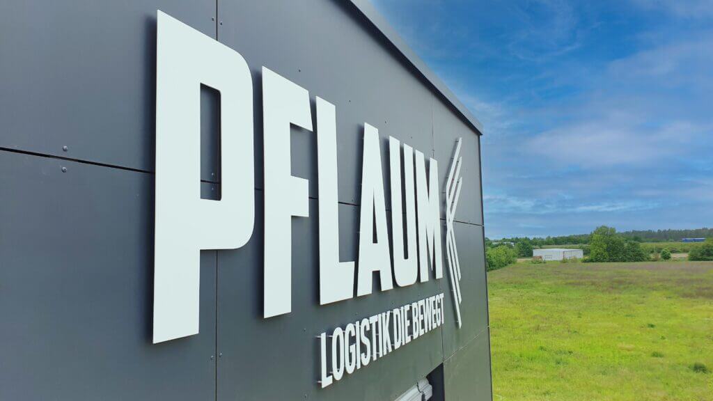 Weiße PFLAUM-Logistik-Fassadenbuchstaben an einer grauen Industriehalle