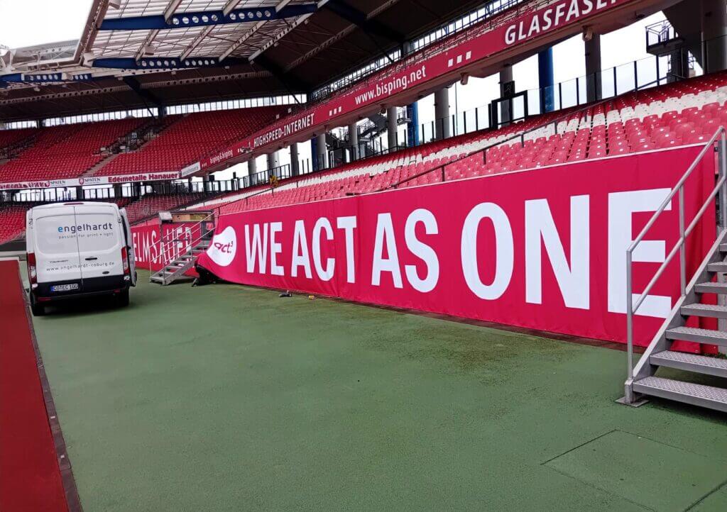 Rote Stadionbande mit dem Schriftzug „We act as one“ im Max-Morlock-Stadion Nürnberg